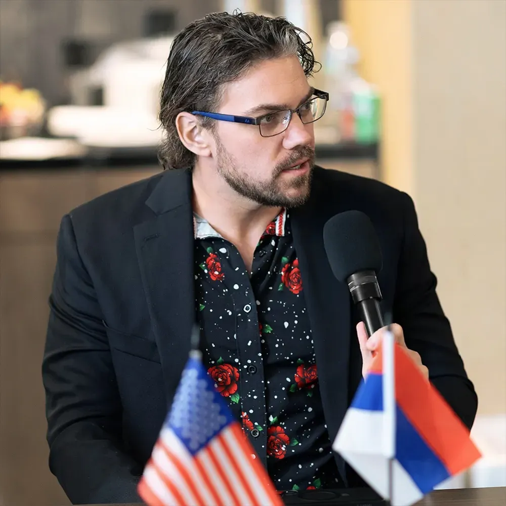 Michael Griswold speaking into a microphone, with US and other flags in the foreground.